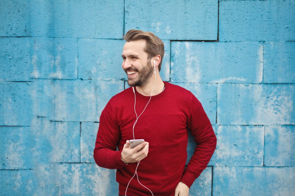 赤のロンTで携帯で音楽を聴きながら笑顔の男性