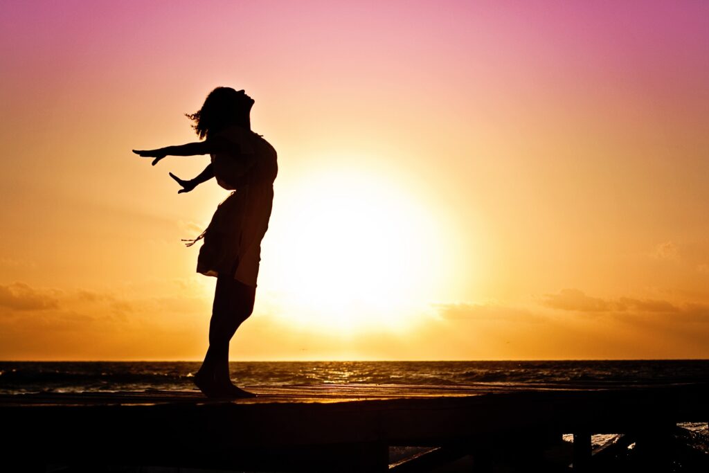 女性が海辺で夕陽をバックに手を広げてる姿